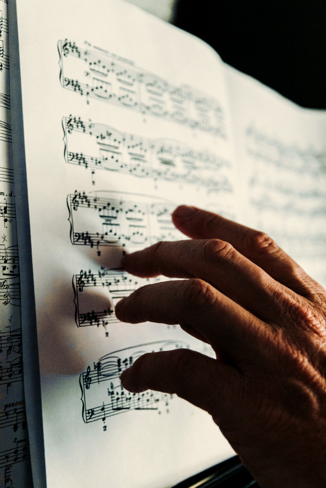 Older person's hand pointing at the notes on a piece of sheet music.